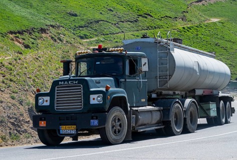 A green truck with a tank trailer is driving on a mountain road, Mack truck with Iranian license