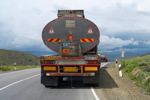 A truck drives on a winding road through a mountainous landscape under cloudy sky, truck with