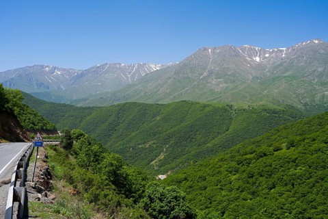 A winding mountain road snakes through green hills with mountains in the background, landscape on