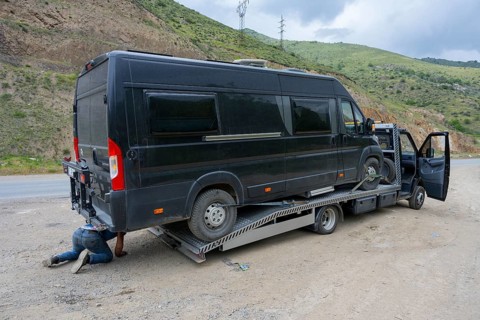 Black van on a car transporter, driver working under the vehicle, camper being towed, motorhome,