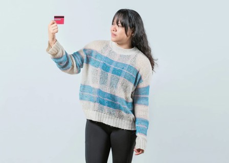 Confused asian girl holding a credit card isolated. Unsure and confused young woman holding and