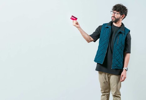 Confused modern guy holding a credit card isolated. Unsure and confused young man holding and