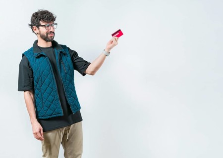 Unsure and confused young man holding and looking at a credit card. Confused modern guy holding a
