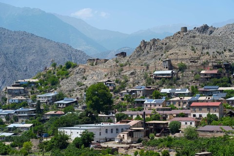 Hilly landscape with a village using solar panels, surrounded by rocky mountains in sunny weather,