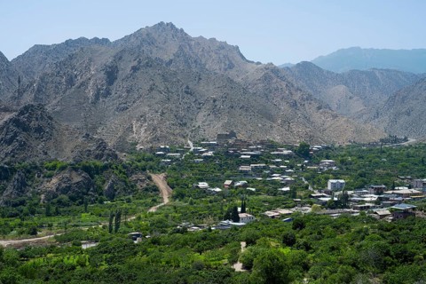Mountain village with lush vegetation, surrounded by imposing mountains and clear blue sky, Meghri,