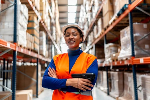 Smiling black woman worker wearing safety vest and hard hat, holding a scanner while standing with