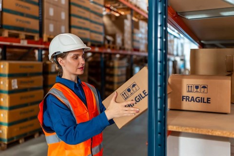 Worker in safety gear handling a fragile package, organizing inventory on a shelf in a modern