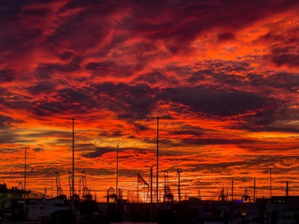 Dramatic sunset sky at Hamburg's Landungsbrücken with silhouetted cranes, ship masts and wind