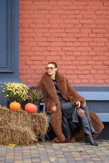 A woman sits on a bench dressed in warm fur coat. She poses near colorful pumpkins and vibrant