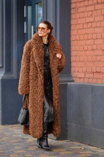 A fashionable woman strolls along a city sidewalk wearing a warm brown fur coat and stylish black