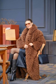 A stylish woman sits at an outdoor cafe during autumn, wearing a fuzzy brown coat and black