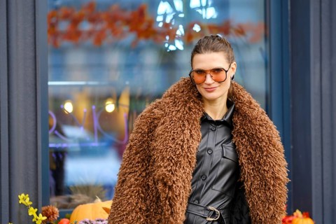 Fashionable woman in stylish brown fur coat posing outside a modern cafe on a sunny autumn day