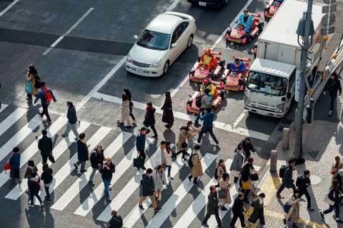 People cross zebra crossings, people in costumes ride small go-kart racing cars, Shibuya Crossing,