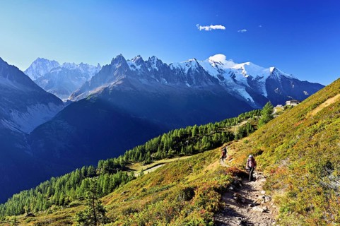Female hiker on a hiking trail with the La Flégère cable car mountain station and the snow-covered