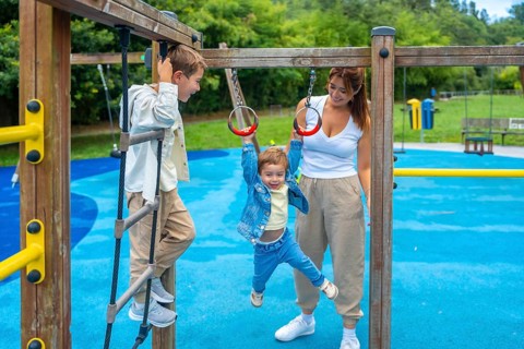Two brothers and their mother are having fun on a playground jungle gym, with one child climbing a