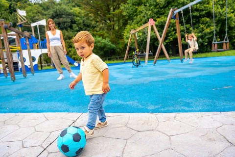 Happy toddler kicking a vibrant soccer ball at the playground, with mother and sister enjoying