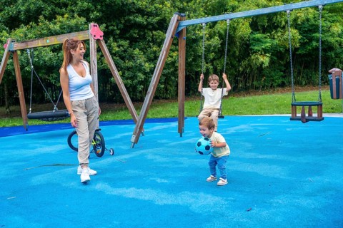 Mother enjoying a sunny day at the playground, watching her children happily playing with a ball