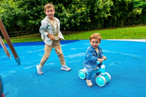 Two brothers are spending time together on a playground, one riding a balance bike and the other