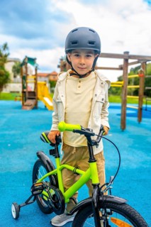 Happy boy wearing helmet learning to ride a bicycle with training wheels in a playground on a sunny