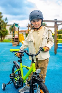 Young boy wearing a helmet standing and holding the handlebars of his bicycle with training wheels