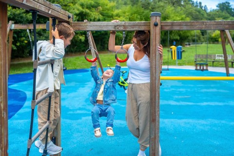 Mother watching children playing joyfully on monkey bars at the playground, fostering family