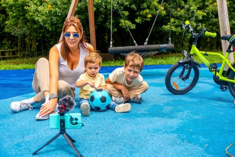 Content creator mother filming video with her sons and a soccer ball on a playground with a swing