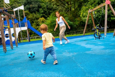 Happy toddler playing soccer with his mother at the playground on a sunny summer day, enjoying