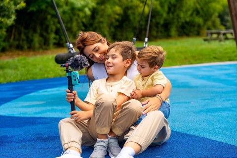 Mother and two sons are sitting on playground's rubber surface, holding a smartphone attached to a