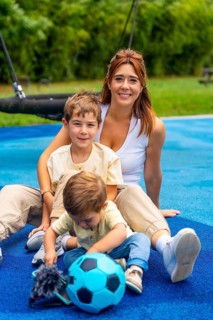 Mother and her two sons are sitting on a playground's blue rubberized surface, enjoying quality