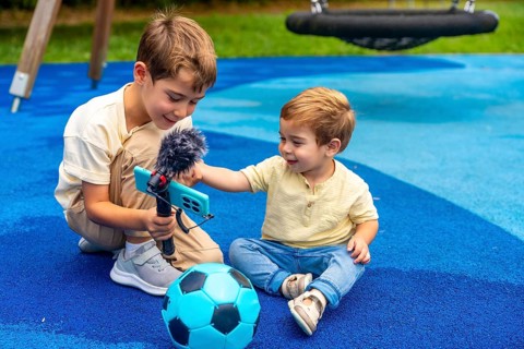 Two brothers playing as videobloggers in the playground, capturing fun moments with their phone and