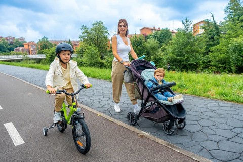 Young mother pushing a stroller with her baby boy, while her older son rides a bicycle with a
