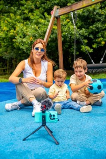 Content creator filming a video with two children at a playground, using a smartphone, microphone,