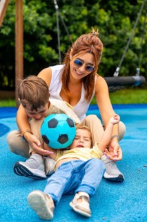 Happy mother and two children playing with a soccer ball on a playground's blue rubberized surface,
