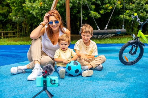 Influencer mother vlogging with her two children at the playground, capturing joyful moments with a