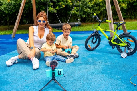 Influencer mother recording a video with her two sons at playground using a smartphone and