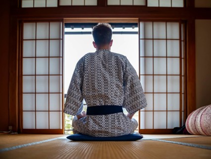 Young man wearing kimono sitting in traditional Japanese living room with tatami mats and shoji