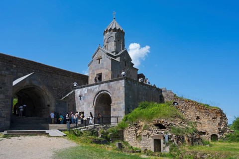 Historic stone church with ruins and grassy areas under clear blue sky, Tatev monastery, Armenian