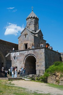 Popular chapel with tower and group of visitors under blue sky, Tatev monastery, Armenian Apostolic