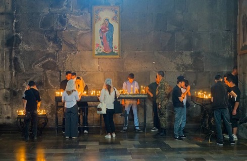 People gather in a church praying, surrounded by burning candles and murals, in a thoughtful mood,