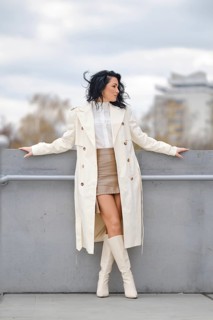 A woman showcases her autumn street style while standing on a balcony. She wears a long white coat