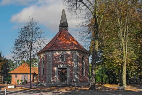Brick chapel with pointed roof and roof turret, surrounded by autumn trees under a blue sky,