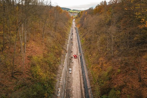 Aerial view of a construction site in an autumnal forest, with a long area of soil between steep