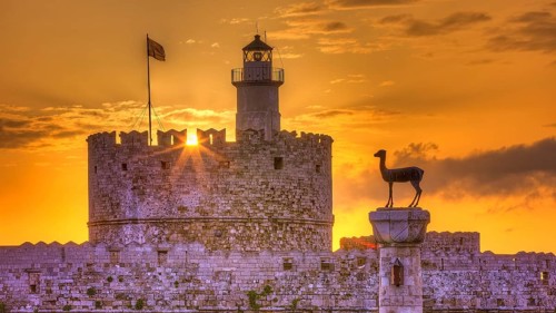 Agios Nikolaos fortress, castle with lighthouse and statue in rising sun and golden sky, UNESCO
