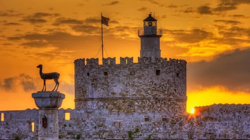 Agios Nikolaos fortress, historic castle with statue in front of a warm sunrise sky, UNESCO World