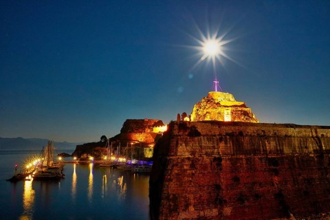 Old fortress, illuminated fortress at night with cross and starry sky over quiet harbor, UNESCO