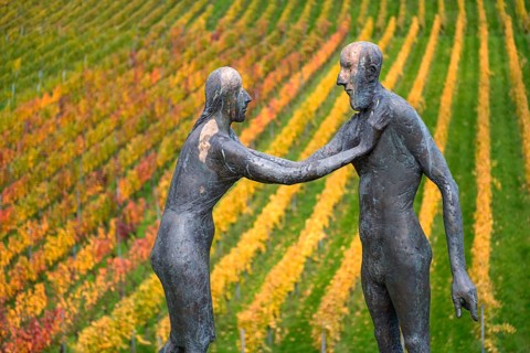 Two human figures as sculptures stand in front of colorful vines in an autumnal atmosphere,