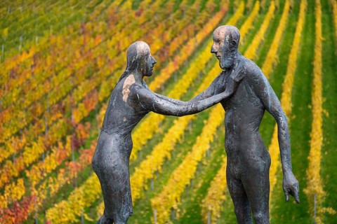 Sculpture of two people in front of colorful vines in autumn, emphasized by artistic