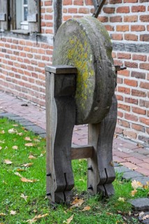 Old whetstone on wooden stand surrounded by grass and brick buildings, Münsterland, North