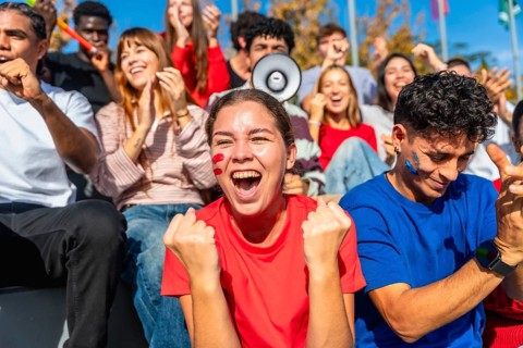 Young diverse fans sitting in a stadium enjoying a sporting event, celebrating and cheering for