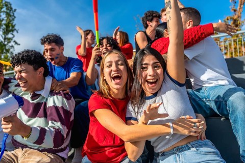 Cheerful young friends sitting in stadium stands, actively cheering and celebrating, enjoying a